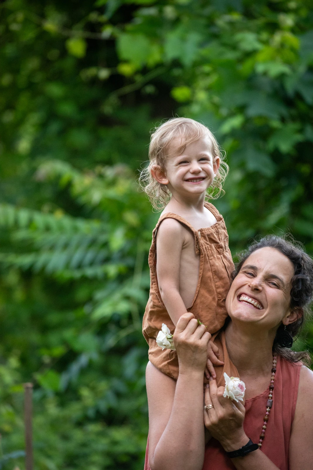 A child playfully touching their mother's nose with a flower petal in a lush Asheville garden